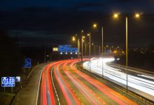 Smart motorway in England, UK with light trails signifying busy traffic at rush hour. The NSL symbols under the gantry sign signify an end to speed restrictions.