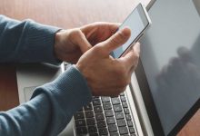 Person holding phone near a laptop while getting two-factor authentication info