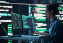 Female Developer Thinking and Typing on Computer, Surrounded by Big Screens Showing Coding Language. Professional Programmer Working in an Office, Running Coding Tests. Futuristic Programming