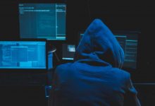 Hacker using computer for organizing massive data breach attack on goverment servers. Hacker in dark room surrounded computers