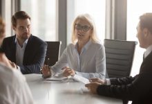 Serious middle aged businesswoman talks at group board executive meeting, confident mature old female leader speaking discussing work offers solution negotiating with partners at corporate briefing