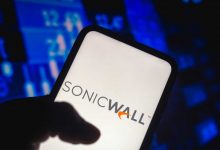 A silhouetted hand holding a smartphone, with the SonicWall logo displayed on the screen.