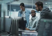 Diverse Multi-Ethnic Team in Modern Office: Teamwork of IT Programmers Gather Around Desktop Computer, Talking, Finding Solution. Specialists Create Software. Engineers Develop App, Program