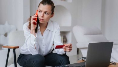 Worried businesswoman talks by phone with bank employee holds credit card sitting at desk with laptop tries to resolve problems, irritated by partners mistakes. Crisis, failure.